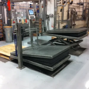 Stainless steel lifting table in the middle of an industrial environment beside another stainless steel table.
