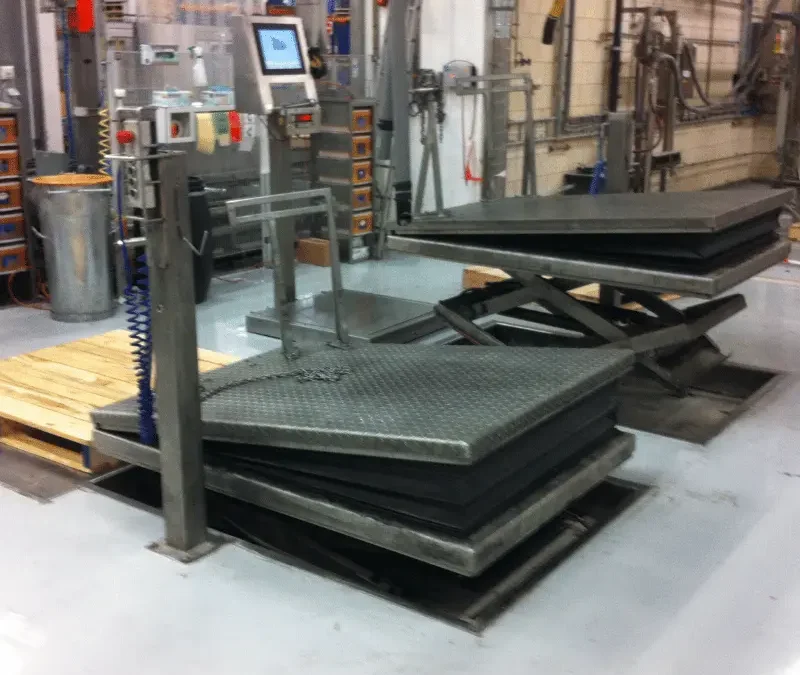 Stainless steel lifting table in the middle of an industrial environment beside another stainless steel table.