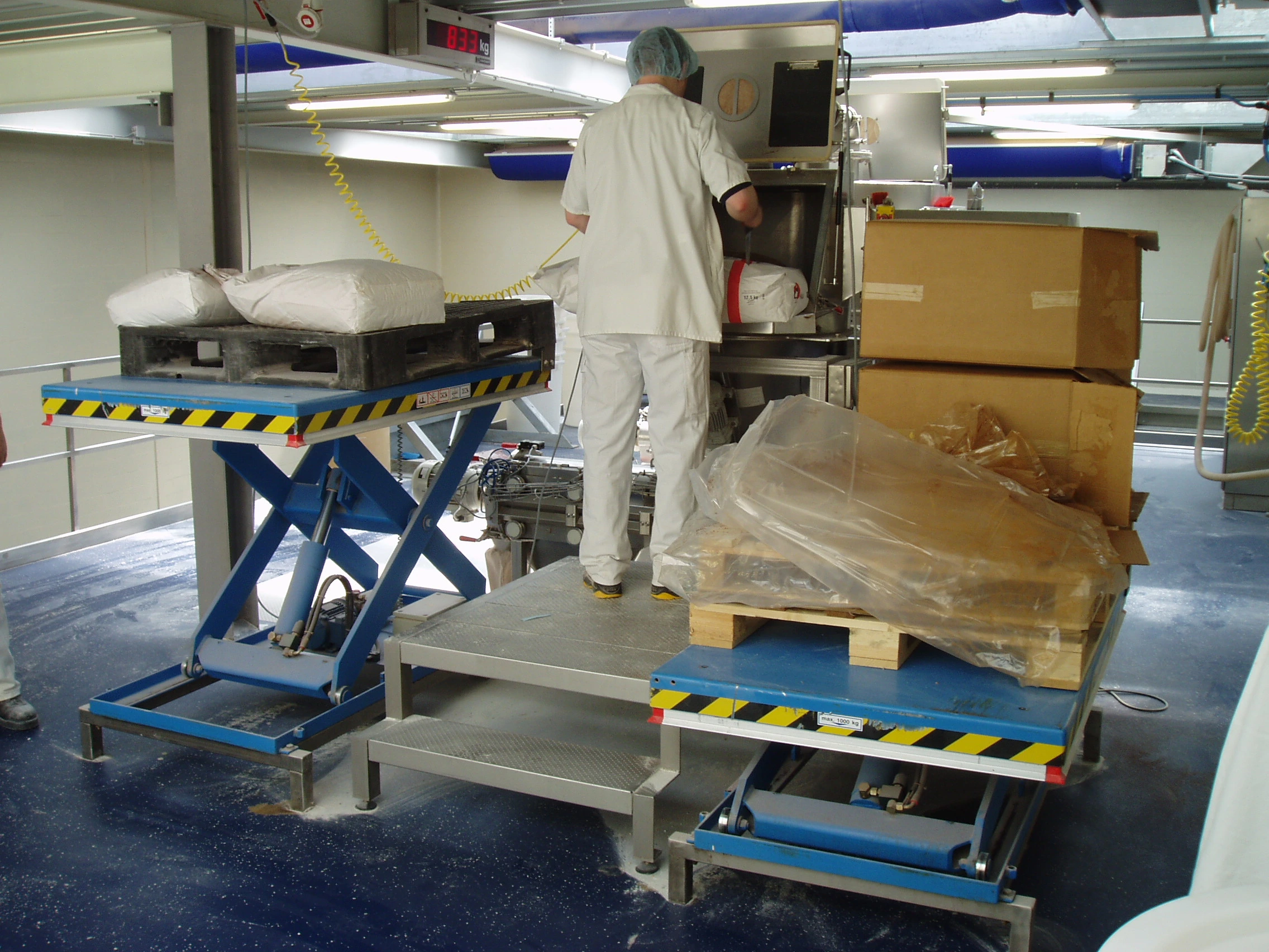 Person working in a warehouse operating two scissor lifts.